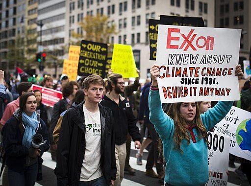 protesters hold signs saying Exxon Knew while marching through city streets