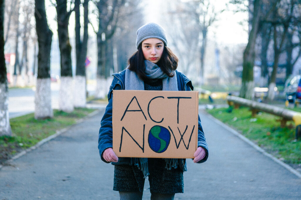 Young woman activist holding a climate change sign that says "Act Now"