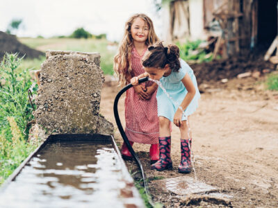 two little girls drinking water out of a hose
